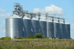 Large agricultural grain storage silos with conveyor systems in rural farmland under blue sky