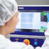Worker in protective gear operating TOLEDO industrial inspection machine with quality control display showing accepted and rejected items