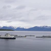 Aquaculture vessel operating among fish farm pens with snow-capped mountains in the background