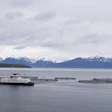 Aquaculture vessel operating among fish farm pens with snow-capped mountains in the background