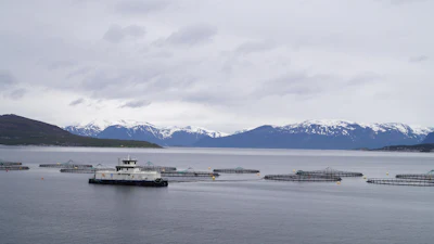 Aquaculture vessel operating among fish farm pens with snow-capped mountains in the background