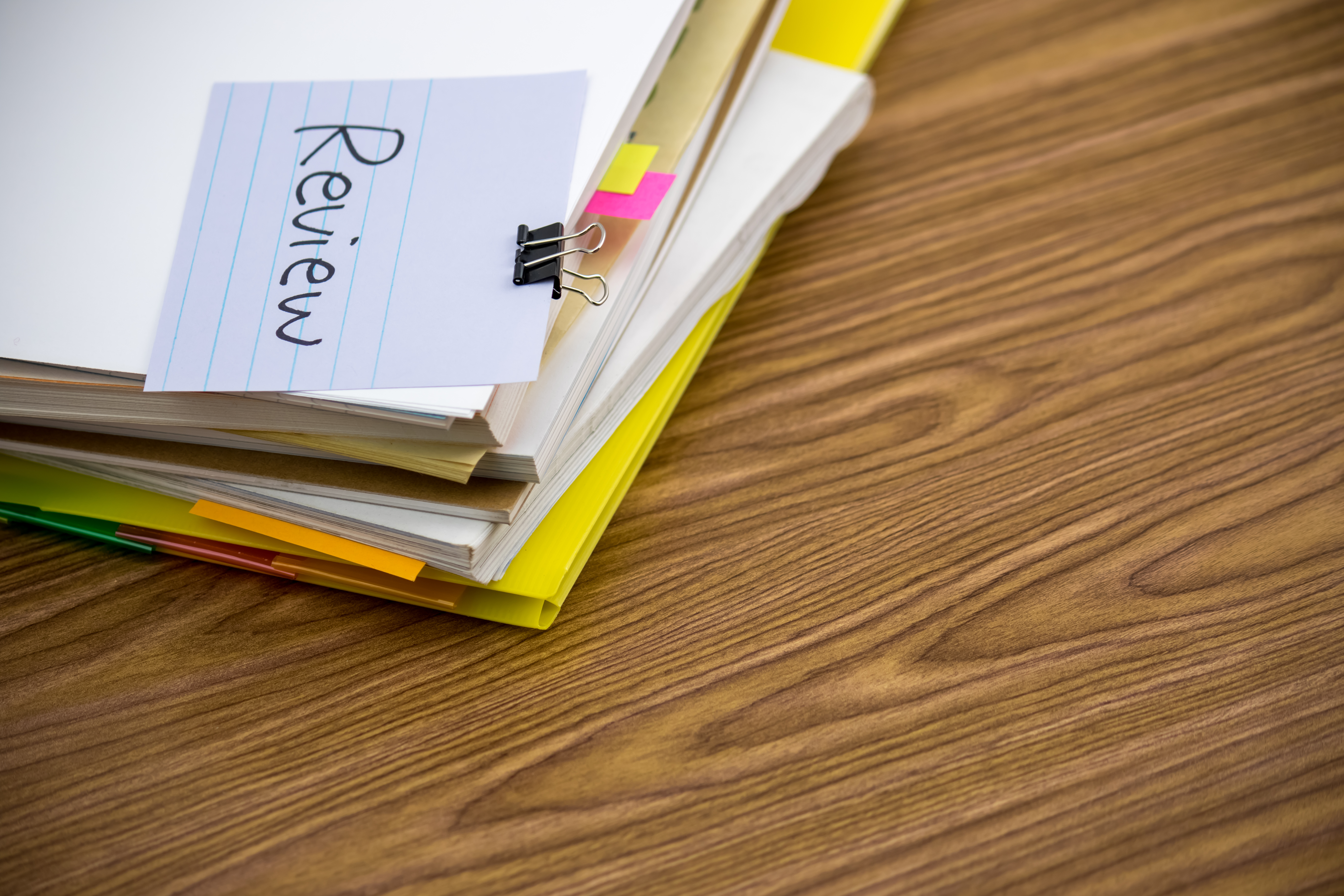 Notebook with 'Review' written on page, yellow highlighter, sticky notes, and binder clip on wooden desk