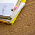 Notebook with 'Review' written on page, yellow highlighter, sticky notes, and binder clip on wooden desk