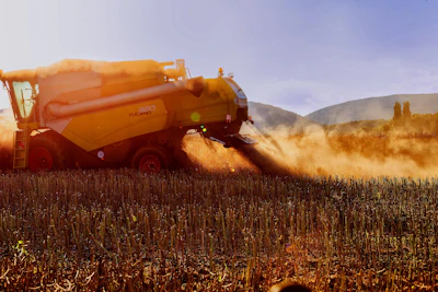 Orange combine harvester harvesting grain in a dusty field with mountains in the background