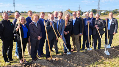 Group of professionals holding shovels at groundbreaking ceremony in rural field with transmission towers in background