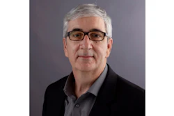 Professional headshot of a man with gray hair wearing glasses and dark blazer over gray shirt