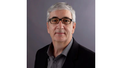 Professional headshot of a man with gray hair wearing glasses and dark blazer over gray shirt