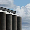 Five cylindrical grain storage silos with metal roof against blue sky and white clouds