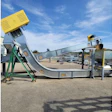 Industrial concrete mixer and conveyor system with yellow hopper and green support frame at outdoor facility