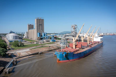 Cargo ship docked at grain elevator facility with loading cranes along industrial waterway