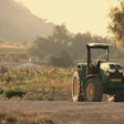 Green tractor parked on rural road with cultivated fields and mountains in golden sunlight