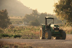 Green tractor parked on rural road with cultivated fields and mountains in misty background at sunset