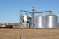 Large grain elevator facility with cylindrical storage silos and conveyor systems in rural farmland