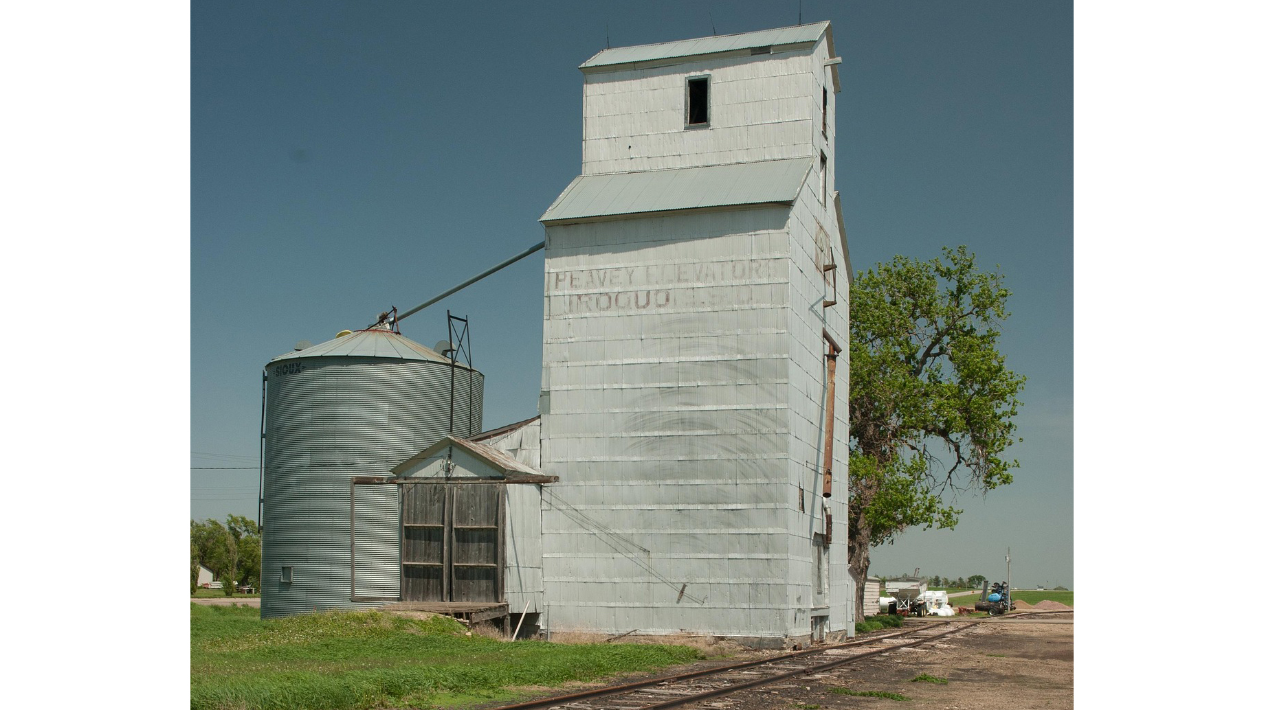 Vintage grain elevator and metal silo in rural farmland under clear blue sky
