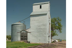 Vintage grain elevator and metal silo in rural farmland under clear blue sky