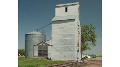 Vintage grain elevator and metal silo in rural farmland under clear blue sky