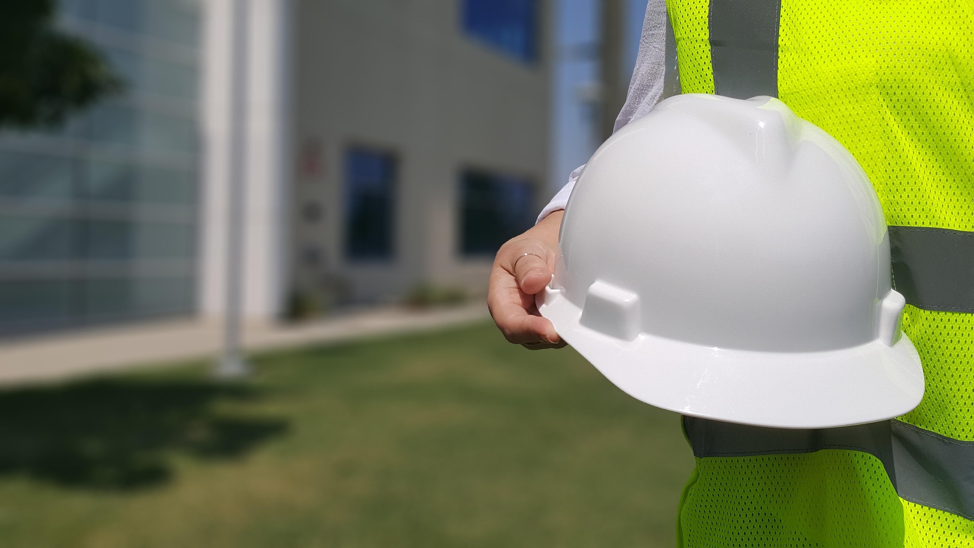 Construction worker in safety vest holding white hard hat on job site