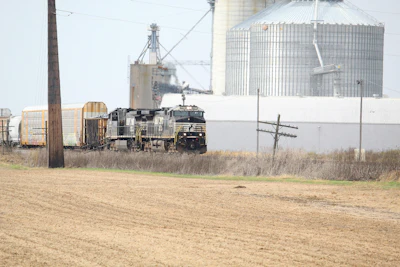Diesel locomotive with freight cars at grain elevator facility in rural agricultural area